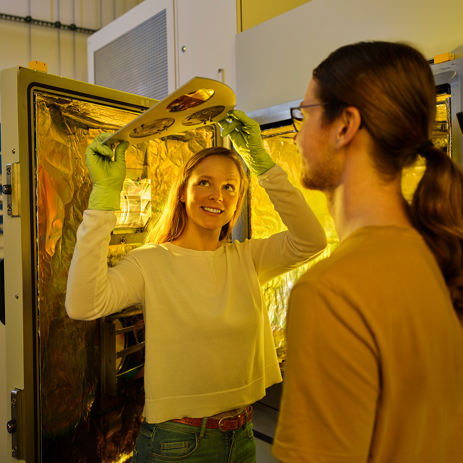 Eine Frau steht vor einem geöffneten Gerät und hält eine Lampe in der Hand. 