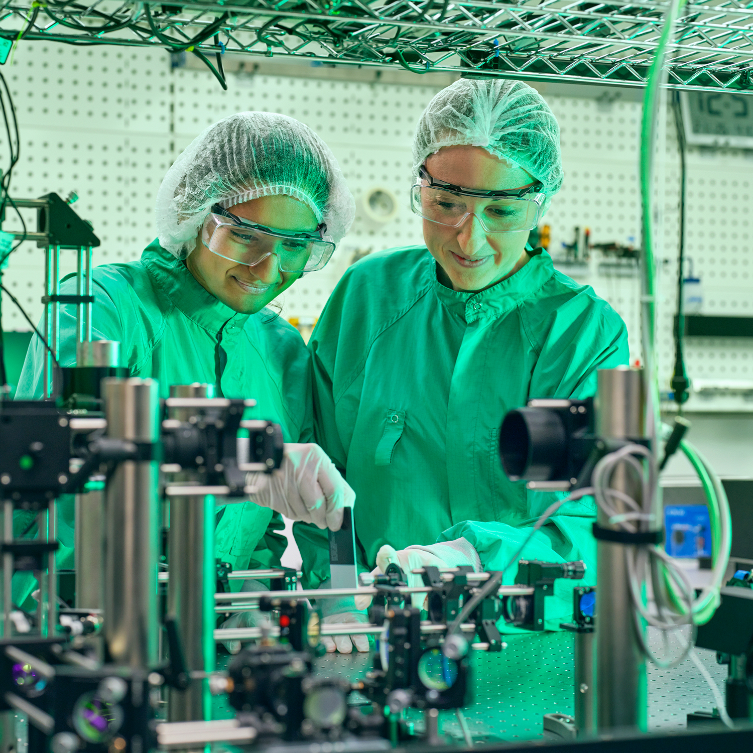 Eine Mann und eine Frau in Schutzkleidung mit Haarnetz arbeiten an einem Laser-System. 