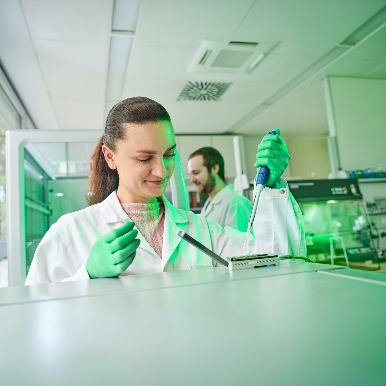 Eine Frau steht in einem Labor und benutzt eine Pipette. 