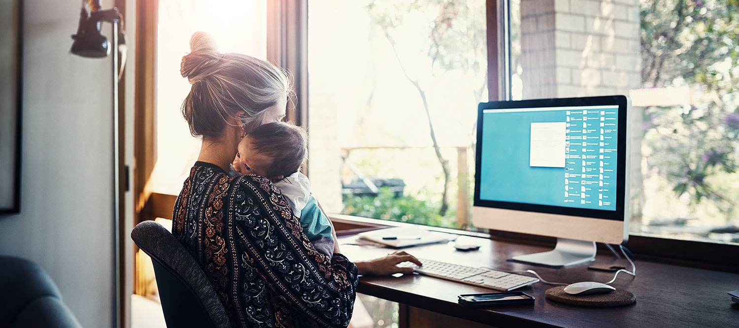 Eine Frau sitzt mit ihrem Baby vor einem PC und arbeitet.